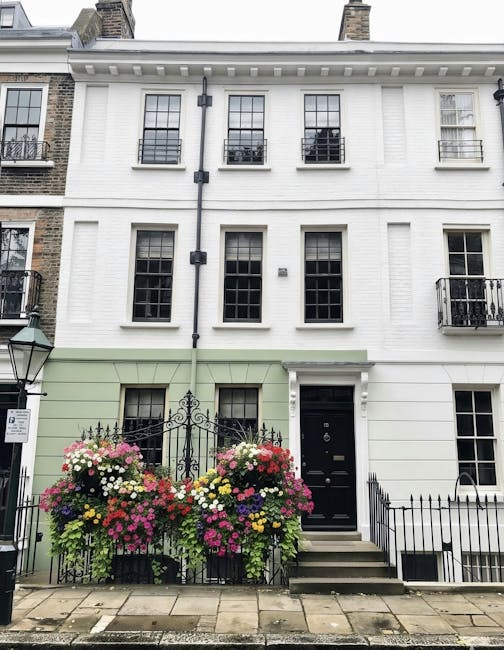 A vibrant floral display outside a white, multi-story townhouse in Fitzrovia, featuring a large arrangement of fresh flowers in shades of pink, white, yellow, and purple, arranged in overflowing baske